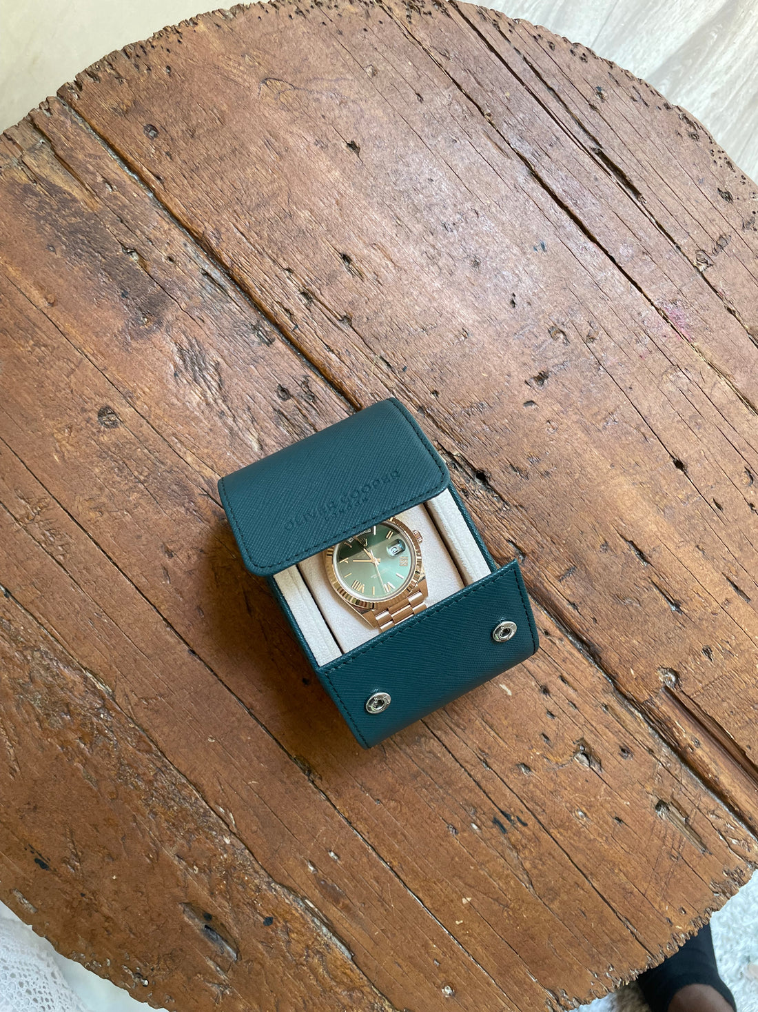 A Rolex watch with a green dial and a gold case, in a green leather case on a table.