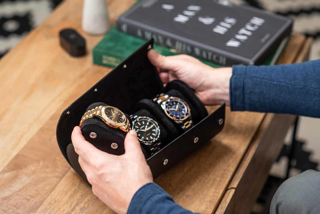  A man's hands opening a black leather watch roll to reveal three luxury watches inside.