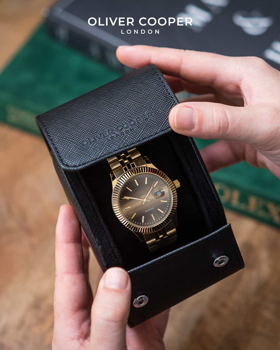 A man's hands opening a black leather watch roll to reveal a gold Rolex watch inside. 