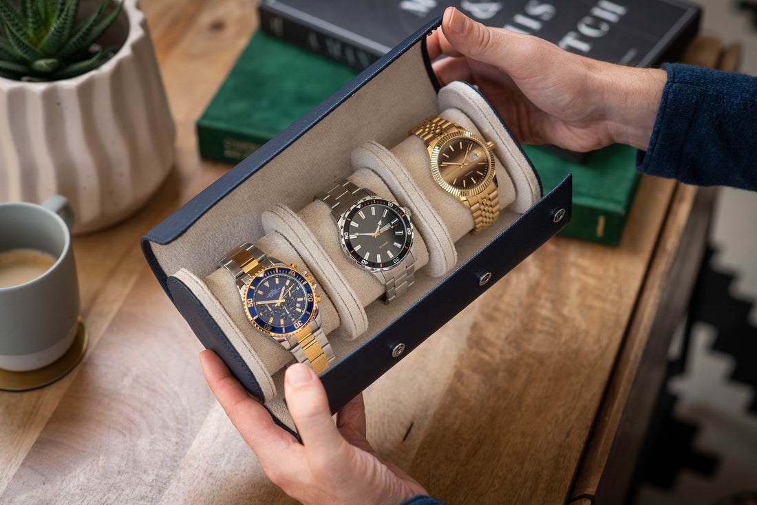 Man's hands opening a blue leather watch roll to reveal three luxury watches