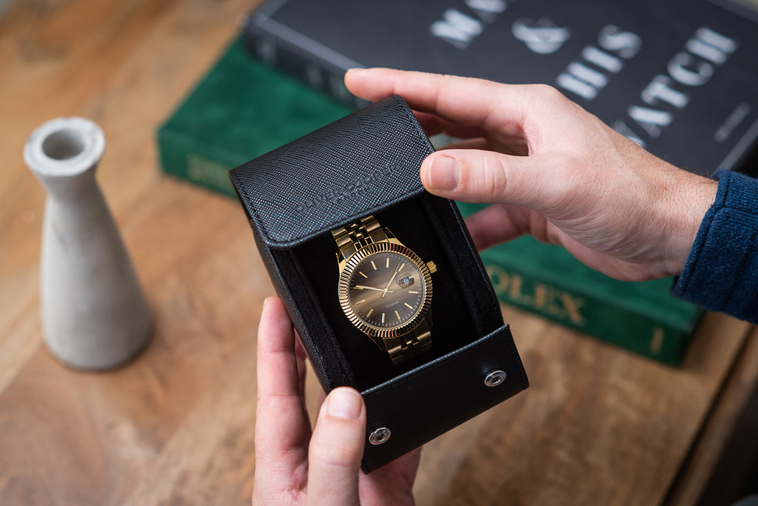 Man's hands opening a black leather watch roll to reveal a gold Rolex watch.