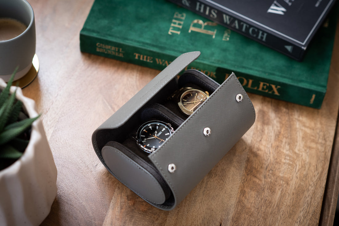 watch roll opened on a table with two watches inside beside two books