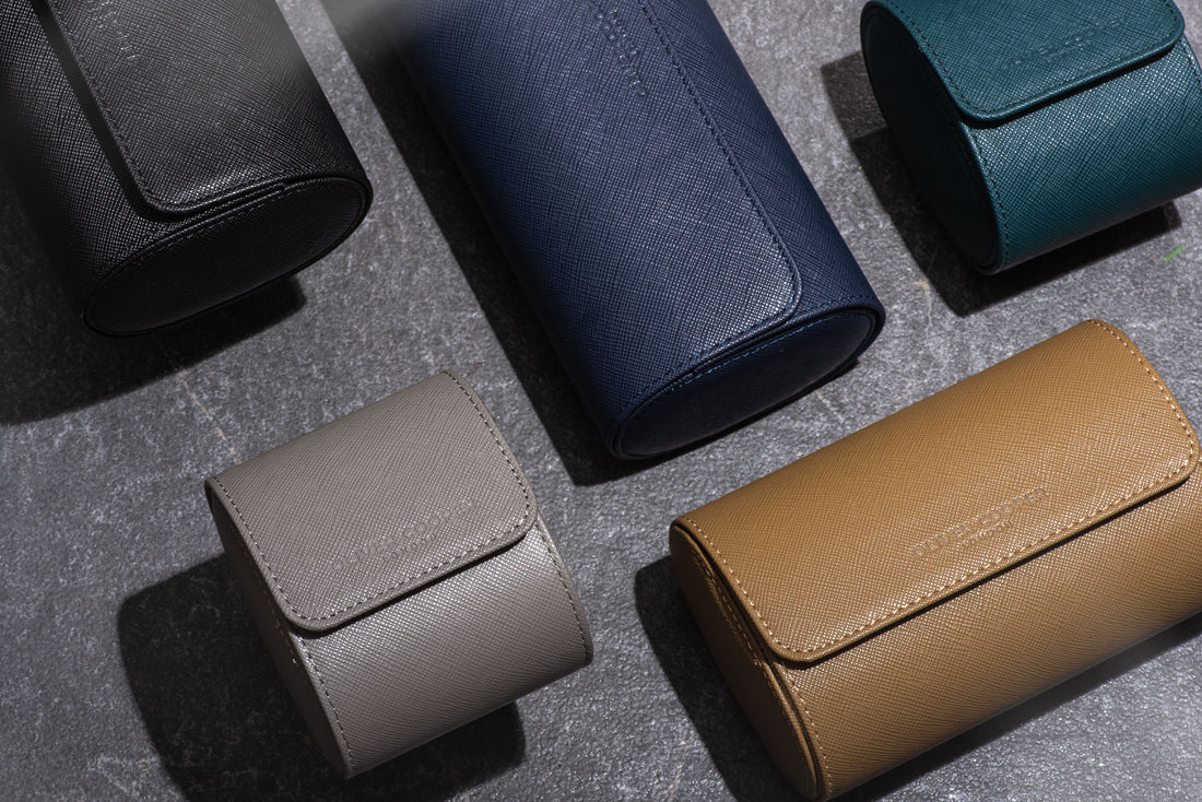  A row of colorful leather watch cases in different shapes and sizes displayed on a gray table. 