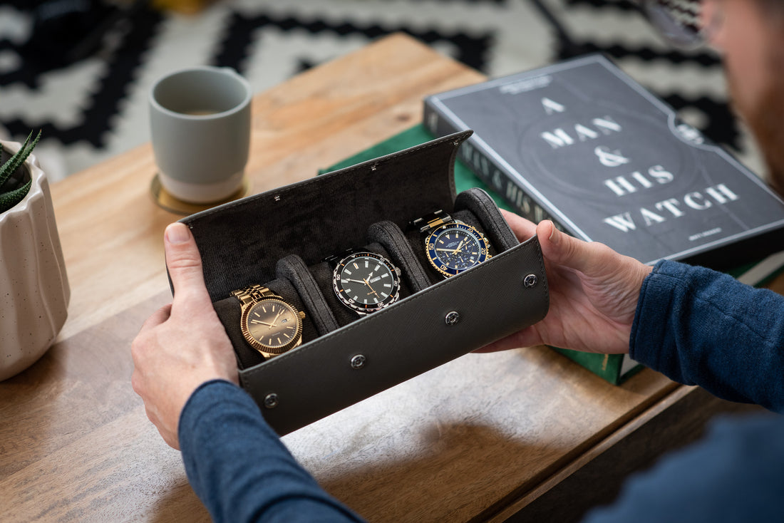 A man is holding a grey leather watch roll with three watches inside.