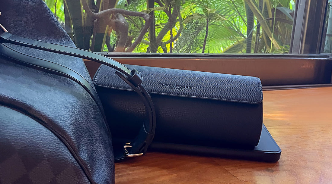 a black leather three watch travel case in a vacation setting. green trees in the background. A louis vuitton duffle bag showing