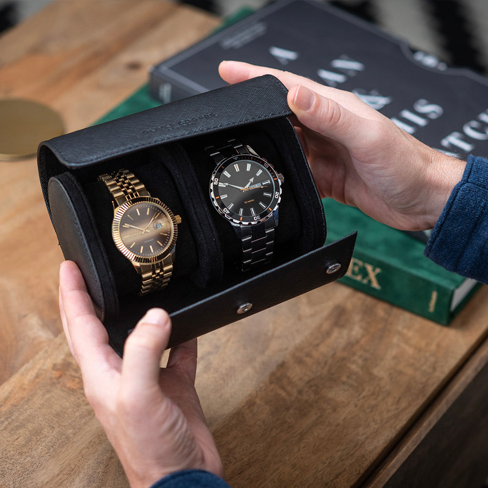 Man holding a black travel watch case with two watches inside: a gold watch and a black watch.