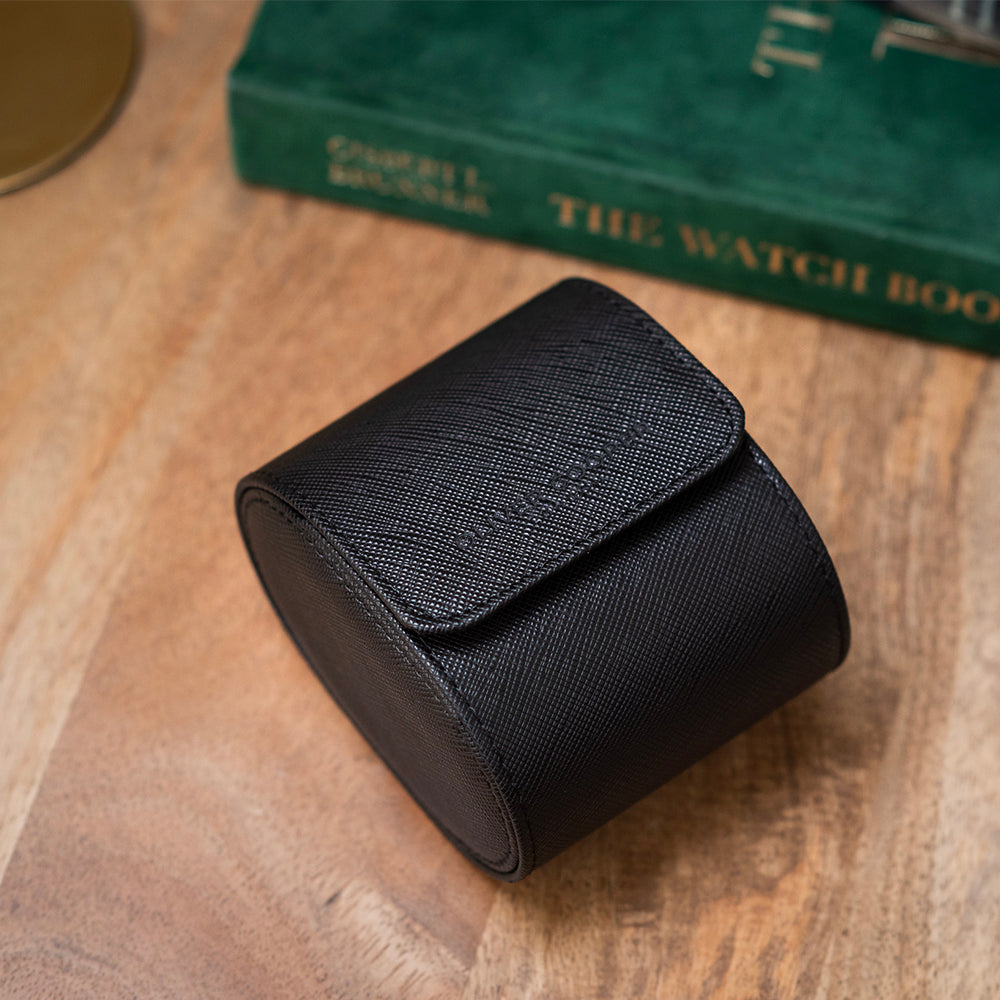 Single black watch holder placed on a wooden table alongside a green Rolex book.