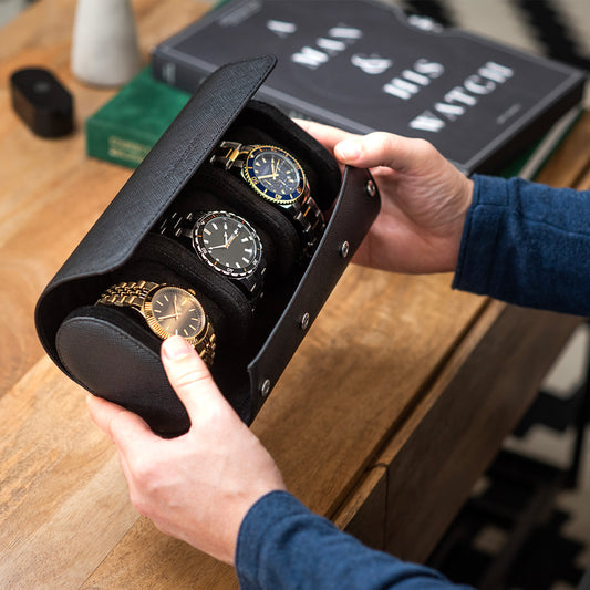 A man holding an open watch roll case with three watches displayed inside.