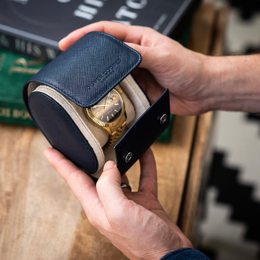 Man holding a navy blue saffiano leather travel case with a gold watch inside its beige interior.