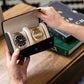 Man opening a Saffiano leather watch roll case for watch display, revealing a gold watch and a silver watch.