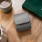 Grey single watch roll case on a wooden table, accompanied by a mug and a green Rolex book.