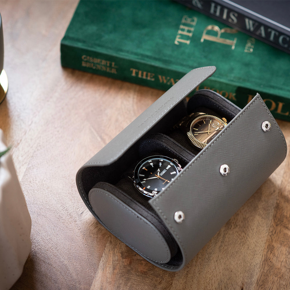 Open watch case on a wooden desk presenting two elegant timepieces: a gold watch and a silver watch.