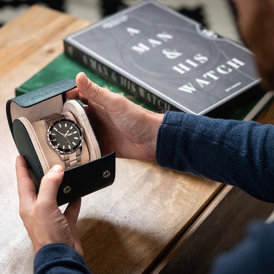 Luxury watch case with a teal saffiano leather exterior, cream suede interior, and a silver watch inside.